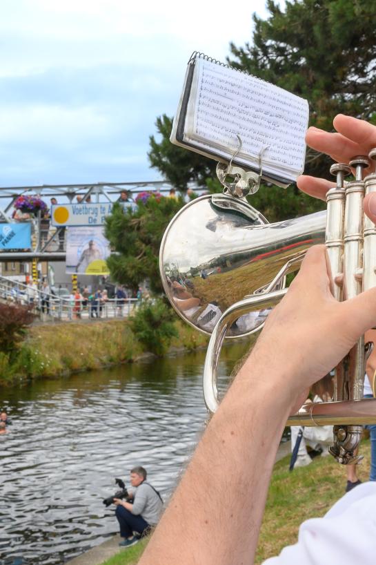Trompetspeler speelt en kijkt in de richting van het kanaal en de voetgangersbrug in Adinkerke.